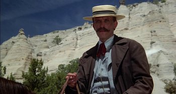 Movie still from “Butch and Sundance: The Early Days” (1979), directed by Richard Lester – A man with a mustache wearing a hat and holding a bag; Medium shot, Low angle
