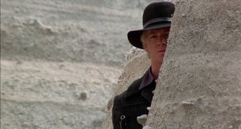 Movie still from “Butch and Sundance: The Early Days” (1979), directed by Richard Lester – A woman wearing a black hat standing next to a rock wall; Close Up shot, Low angle