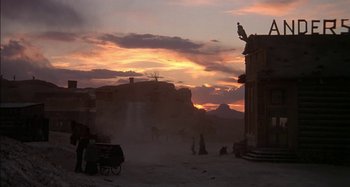 The sun is setting over a desert with a horse drawn carriage