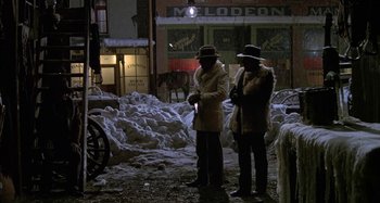 Movie still from “Butch and Sundance: The Early Days” (1979), directed by Richard Lester – Two men standing on the sidewalk in front of a building; Wide shot, High angle