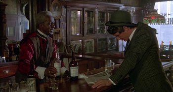 Movie still from “Butch and Sundance: The Early Days” (1979), directed by Richard Lester – Two men sitting at a table in front of a newspaper; Medium shot, Over the shoulder angle