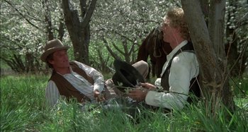 Movie still from “Butch and Sundance: The Early Days” (1979), directed by Richard Lester – Two men sitting in the grass near a horse; Medium shot, Over the shoulder angle