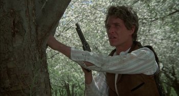 Movie still from “Butch and Sundance: The Early Days” (1979), directed by Richard Lester – A man holding a gun up to the side of a tree; Close Up shot, Low angle