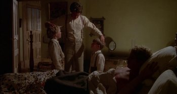 Movie still from “Butch and Sundance: The Early Days” (1979), directed by Richard Lester – A man standing next to two young boys in front of a bed; Medium shot, Over the shoulder angle