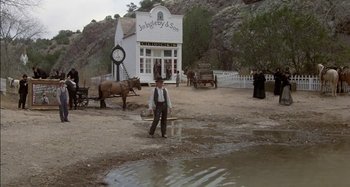 Movie still from “Butch and Sundance: The Early Days” (1979), directed by Richard Lester – A man standing in front of a building with a horse drawn carriage; Wide shot, Low angle