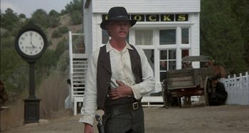 Movie still from “Butch and Sundance: The Early Days” (1979), directed by Richard Lester – A man holding a gun in front of a building; Medium shot, Low angle