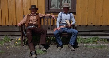 Movie still from “Butch and Sundance: The Early Days” (1979), directed by Richard Lester – A couple of men sitting on top of a wooden bench; Wide shot, Low angle