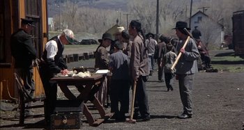Movie still from “Butch and Sundance: The Early Days” (1979), directed by Richard Lester – A group of people standing around a table; Wide shot, High angle