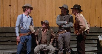 Movie still from “Butch and Sundance: The Early Days” (1979), directed by Richard Lester – A group of men sitting next to each other on a bench; Medium shot, Low angle