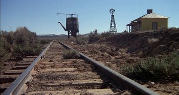 Movie still from “Butch and Sundance: The Early Days” (1979), directed by Richard Lester – An old windmill is in the background of an old train track; Extreme Wide shot, Low angle