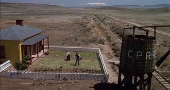 Movie still from “Butch and Sundance: The Early Days” (1979), directed by Richard Lester – A man standing in a field next to a fence; Extreme Wide shot, High angle