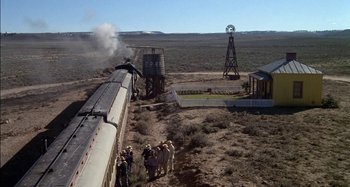 Movie still from “Butch and Sundance: The Early Days” (1979), directed by Richard Lester – A group of people standing next to a train on a train track; Extreme Wide shot, High angle