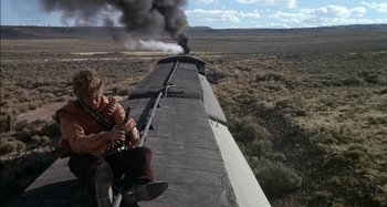 Movie still from “Butch and Sundance: The Early Days” (1979), directed by Richard Lester – A man sitting on the side of a train while smoke billows out of it; Wide shot, Low angle