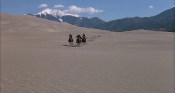 Movie still from “Butch and Sundance: The Early Days” (1979), directed by Richard Lester – A group of people riding horses through the sand dunes; Extreme Wide shot, High angle