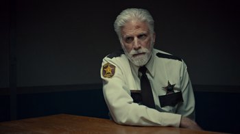 Movie still from “Fargo” (2014), created by Noah Hawley – An older man with a gray beard wearing a sheriff's uniform; Close Up shot, Over the shoulder angle