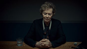 Movie still from “Fargo” (2014), created by Noah Hawley – An older woman sitting at a wooden table with her hands clasped together; Close Up shot, Low angle