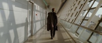 Movie still from “Code 46” (2003), directed by Michael Winterbottom – A man walking down a long hallway with a bag; Wide shot, High angle