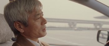 Movie still from “Code 46” (2003), directed by Michael Winterbottom – An older man sitting in the passenger seat of a car; Close Up shot, Over the shoulder angle