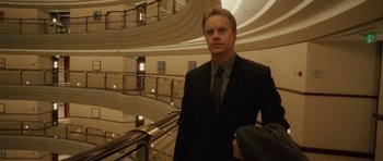 Movie still from “Code 46” (2003), directed by Michael Winterbottom – A man in a suit and tie standing in front of a staircase; Medium shot, Low angle