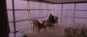 Movie still from “Code 46” (2003), directed by Michael Winterbottom – A man sitting in a chair in front of large windows; Wide shot, High angle