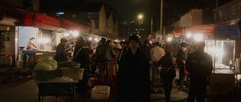 Movie still from “Code 46” (2003), directed by Michael Winterbottom – A group of people standing around a street at night; Wide shot, High angle