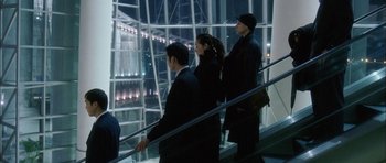 Movie still from “Code 46” (2003), directed by Michael Winterbottom – A group of people riding up a flight of stairs; Wide shot, High angle