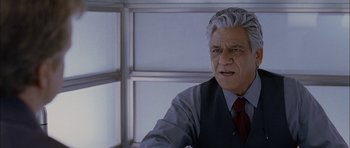 Movie still from “Code 46” (2003), directed by Michael Winterbottom – An older man in a suit and tie looking at the camera; Close Up shot, Low angle