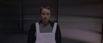 Movie still from “Code 46” (2003), directed by Michael Winterbottom – A woman wearing an apron standing in front of a mirror; Medium shot, Low angle