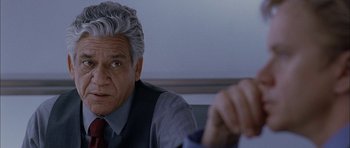 Movie still from “Code 46” (2003), directed by Michael Winterbottom – An older man sitting in front of another man; Close Up shot, Over the shoulder angle