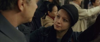 Movie still from “Code 46” (2003), directed by Michael Winterbottom – A woman in a black jacket and a black hat is sitting on a train; Close Up shot, Over the shoulder angle