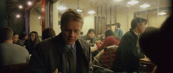 Movie still from “Code 46” (2003), directed by Michael Winterbottom – A man sitting at a table in front of a group of people; Medium shot, Over the shoulder angle