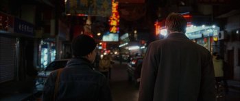 Movie still from “Code 46” (2003), directed by Michael Winterbottom – Two people walking down a street at night; Medium shot, Over the shoulder angle
