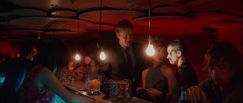 Movie still from “Code 46” (2003), directed by Michael Winterbottom – A group of people sitting at a bar with lights hanging from the ceiling; Medium shot, High angle