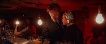 Movie still from “Code 46” (2003), directed by Michael Winterbottom – A man in a suit talking to a woman in a black suit; Close Up shot, Over the shoulder angle