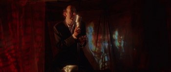 Movie still from “Code 46” (2003), directed by Michael Winterbottom – A man holding a microphone in front of a projected image; Medium shot, Low angle