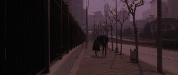 Movie still from “Code 46” (2003), directed by Michael Winterbottom – Two people walking down a sidewalk with an open umbrella; Wide shot, High angle