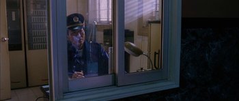 Movie still from “Code 46” (2003), directed by Michael Winterbottom – An older man in a uniform smoking a cigarette in front of a window; Medium shot, Low angle