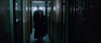 Movie still from “Code 46” (2003), directed by Michael Winterbottom – A woman standing next to a man in a dark room; Wide shot, Low angle