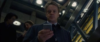 Movie still from “Code 46” (2003), directed by Michael Winterbottom – A man looking at his cell phone while wearing a suit and tie; Close Up shot, Low angle
