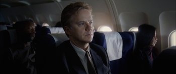 Movie still from “Code 46” (2003), directed by Michael Winterbottom – A man in a suit and tie sitting on a plane; Close Up shot, Low angle