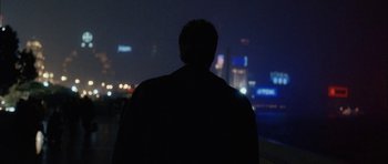Movie still from “Code 46” (2003), directed by Michael Winterbottom – A man standing in front of a city at night; Medium shot, Over the shoulder angle