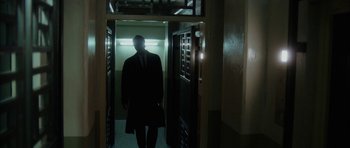 Movie still from “Code 46” (2003), directed by Michael Winterbottom – A man wearing a suit and tie walking through a hallway; Wide shot, Low angle