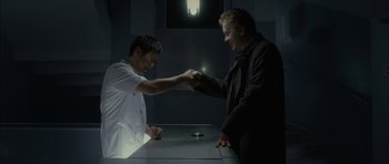 Movie still from “Code 46” (2003), directed by Michael Winterbottom – Two men shaking hands in a dark room; Medium shot, Low angle