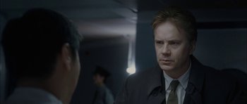 Movie still from “Code 46” (2003), directed by Michael Winterbottom – A man wearing a suit and tie in a room; Close Up shot, Over the shoulder angle