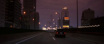 Movie still from “Code 46” (2003), directed by Michael Winterbottom – A car driving down a street at night with lights on; Extreme Wide shot, Low angle