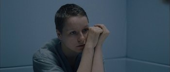 Movie still from “Code 46” (2003), directed by Michael Winterbottom – A woman with short hair is sitting with her head resting on her hands; Close Up shot, High angle