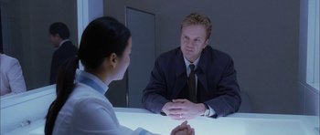 Movie still from “Code 46” (2003), directed by Michael Winterbottom – A man and a woman sitting at a table talking to each other; Medium shot, Over the shoulder angle
