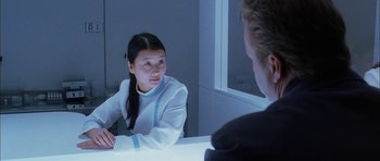 Movie still from “Code 46” (2003), directed by Michael Winterbottom – A woman sitting in front of a mirror talking to a man; Medium shot, Over the shoulder angle
