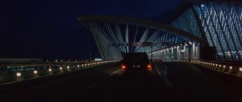 Movie still from “Code 46” (2003), directed by Michael Winterbottom – A car driving down a street at night; Extreme Wide shot, Low angle
