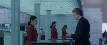 Movie still from “Code 46” (2003), directed by Michael Winterbottom – A man in a suit and tie standing in front of two other women; Medium shot, Over the shoulder angle